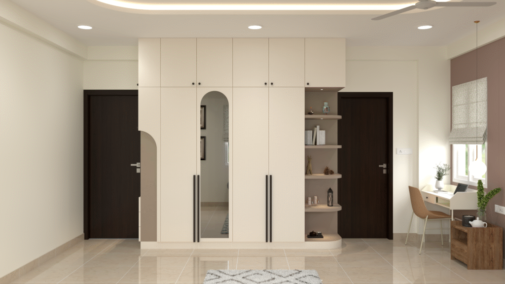 Modern minimalist bedroom with full-height cream wardrobe, arched mirror, black handles, curved open shelves, compact study table by the window and neutral interiors.
