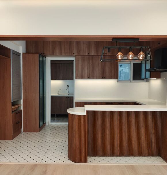 Modern wooden kitchen with fluted breakfast counter, white countertop, pendant lights, wooden cabinets, patterned floor tiles, black framed glass shutters, and open kitchen layout.