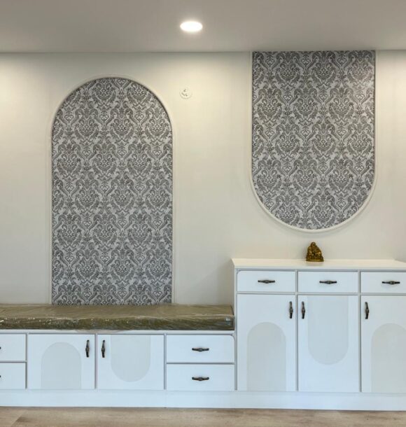 White foyer unit with built-in bay seating, storage cabinets, arched patterned wall panels, drawers, doors, and recessed ceiling lights.