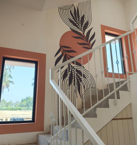 Staircase wall with botanical black line art, terracotta circular accents, terracotta-framed windows, white metal railing, grey steps, and natural light.