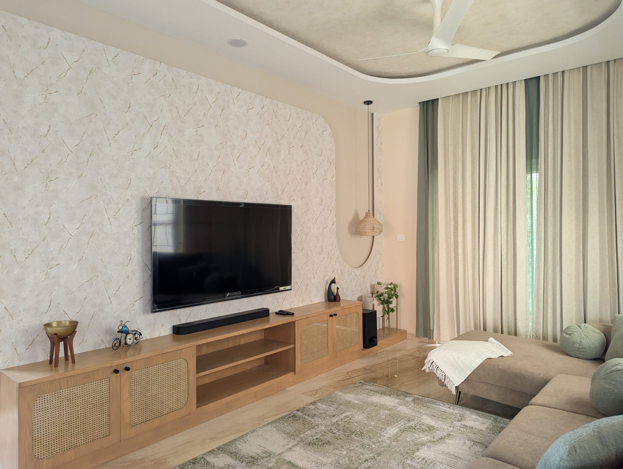 Completed-project living room with textured TV wall, timber media console, neutral sofa and full-height curtains.